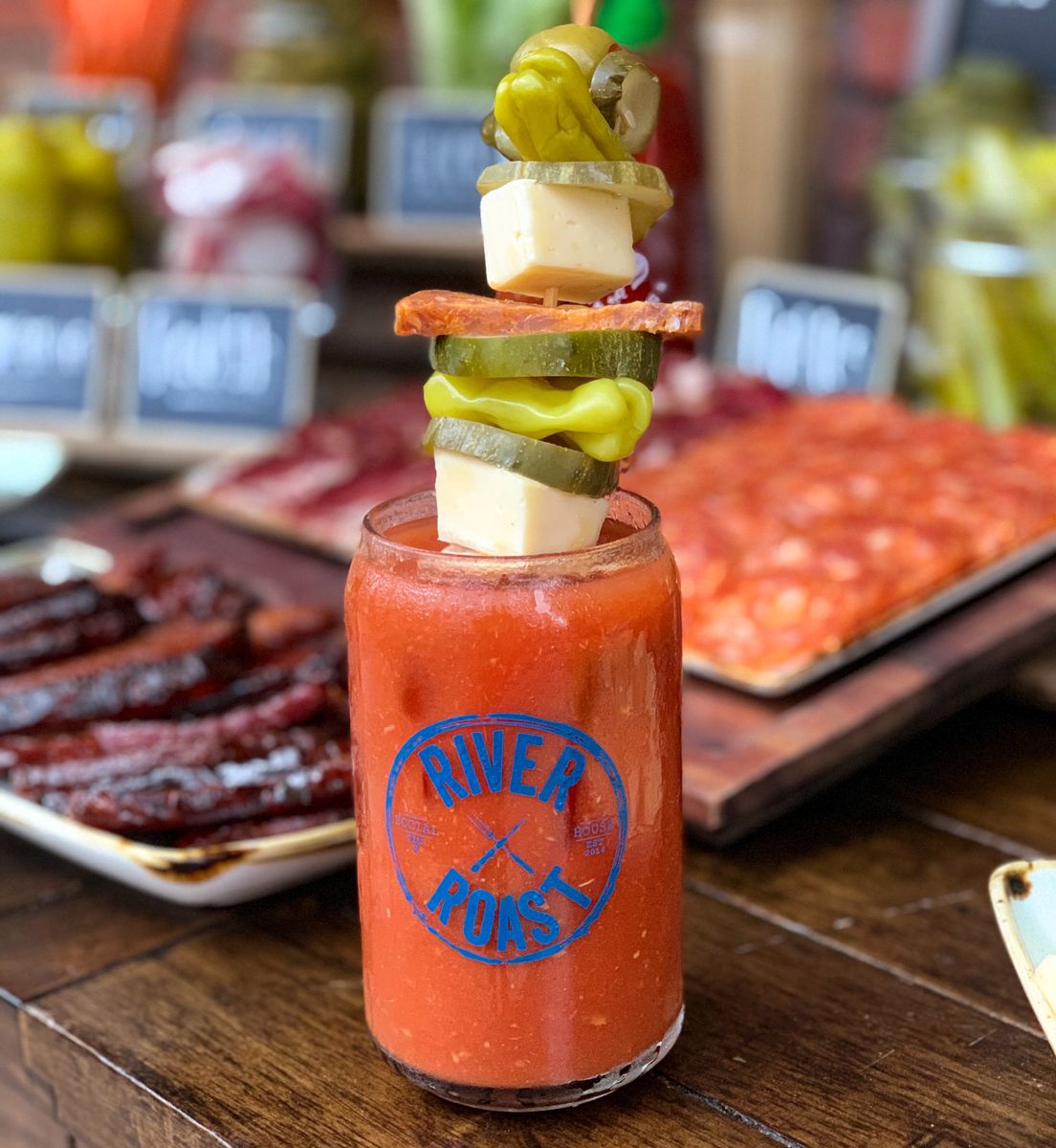 Bloody Mary with a large skewer of cheese chunks, olives, pickled peppers, and salami
